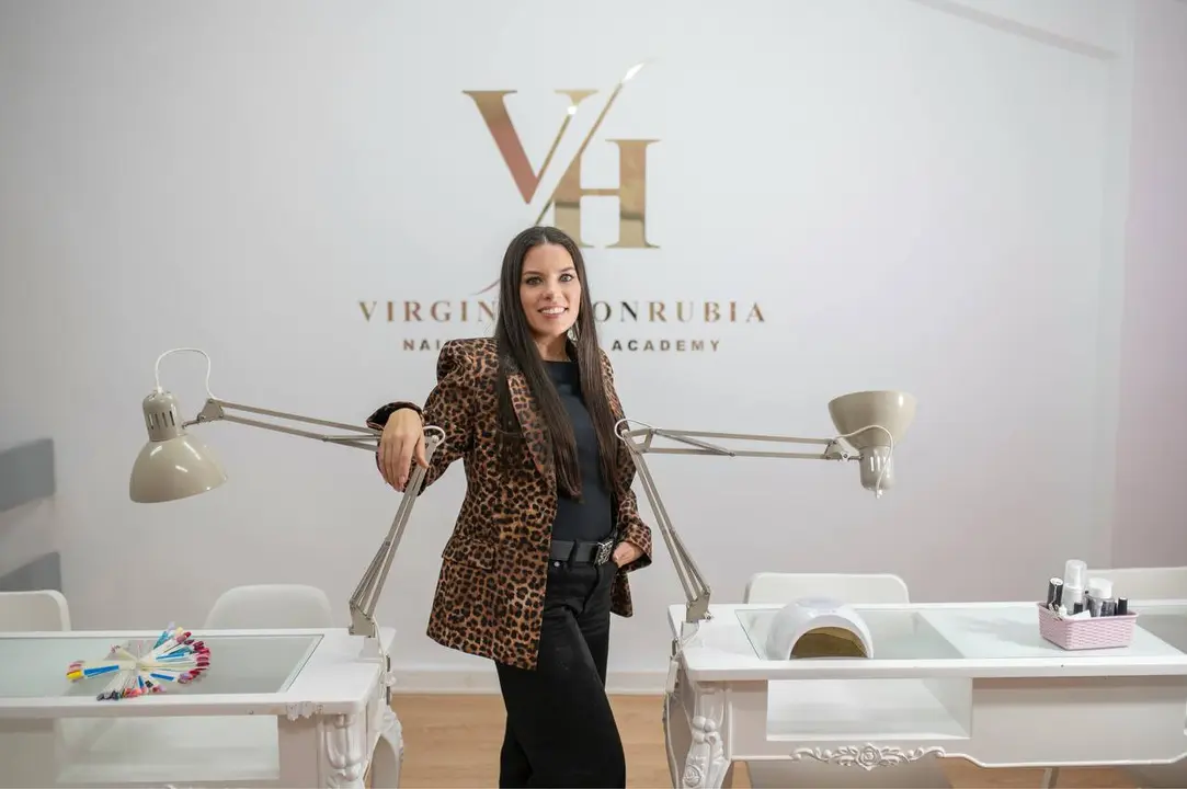 Virginia Honrubia de pie en su sal&oacute;n, junto a las mesas de trabajo donde se realizan manicuras profesionales, mostrando un espacio preparado para ofrecer servicios de u&ntilde;as con calidad y atenci&oacute;n al detalle.