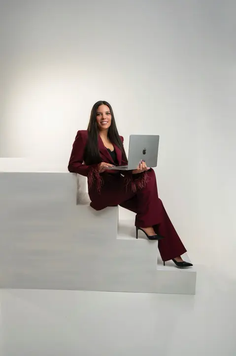 Conoce a Virginia Honrubia, reconocida instructora de formaci&oacute;n en u&ntilde;as, en una foto profesional sentada en escaleras con su ordenador, demostrando su dedicaci&oacute;n y experiencia en la ense&ntilde;anza de t&eacute;cnicas de manicura.