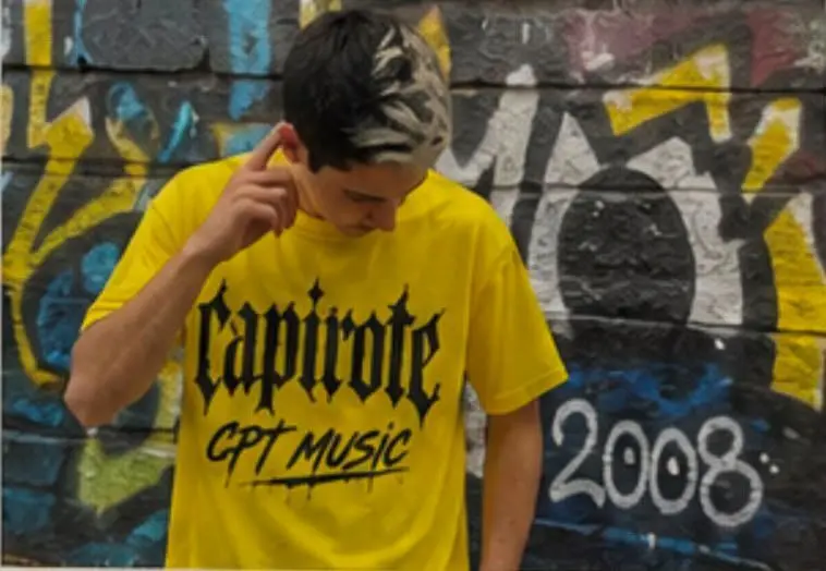 Capirote CPT Music luce una camiseta con su nombre art&iacute;stico frente a un mural de grafitis, una imagen que refleja su apuesta por construir una identidad propia dentro de la escena urbana desde el barrio del Pol&iacute;gono de Toledo.
