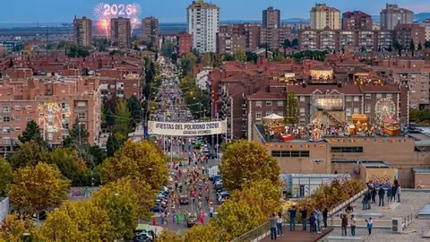 Fotograf&iacute;a a&eacute;rea del barrio del Pol&iacute;gono en Toledo durante las fiestas. La imagen muestra una vibrante celebraci&oacute;n vecinal con un desfile festivo de disfraces en la calle principal, un gran cartel que dice '&iexcl;FIESTAS DEL POL&Iacute;GONO 2026! &iexcl;GRACIAS VECINOS!'
