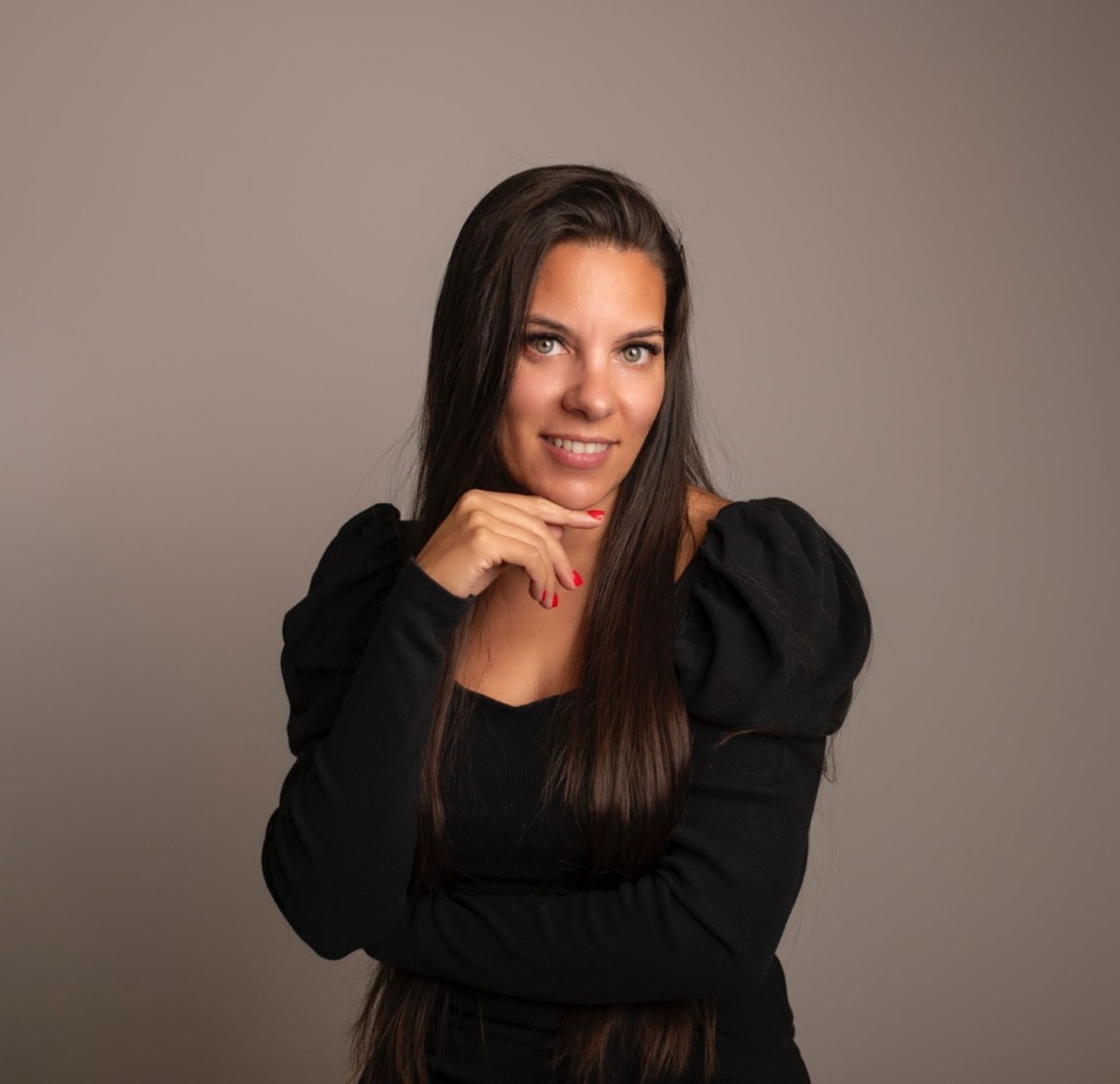 Virginia Honrubia posa de medio cuerpo mirando al frente, sonriendo y con la mano en la barbilla, proyectando seguridad, elegancia y liderazgo como profesional y formadora en el sector de la manicura y la belleza.